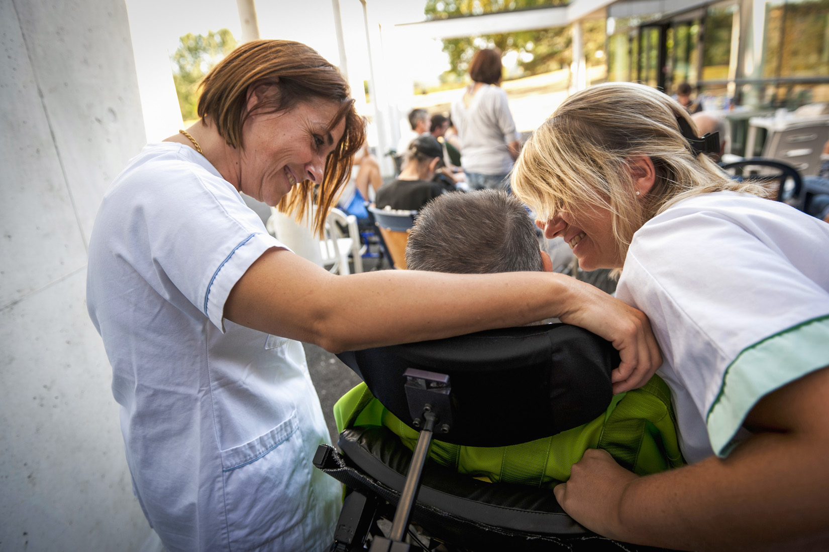 Caregivers smiling at child in wheelchair outdoors