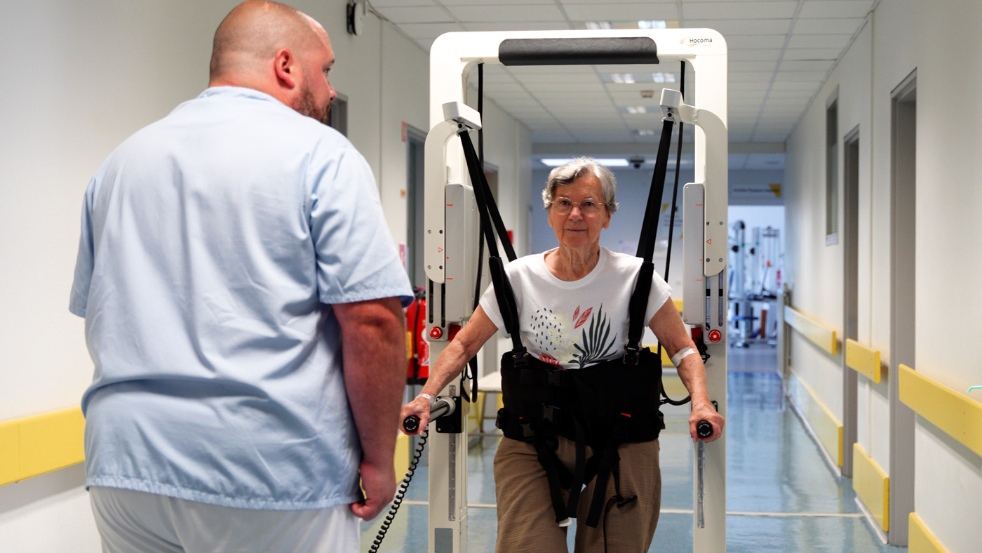 Elderly woman using rehabilitation walking machine with therapist