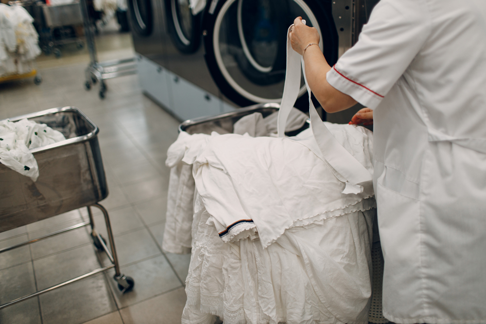 Laundry worker handling white linens in laundromat